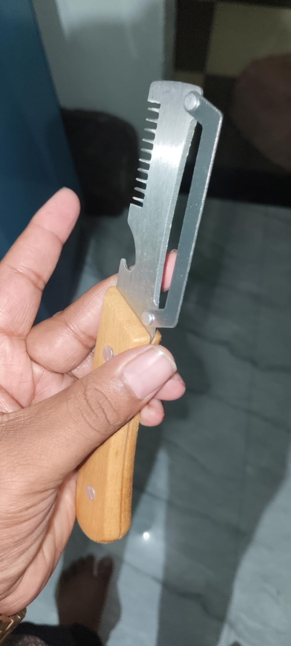 A hand holding a small kitchen tool with a silver metal blade and a light brown wooden handle, photographed in an indoor setting.
