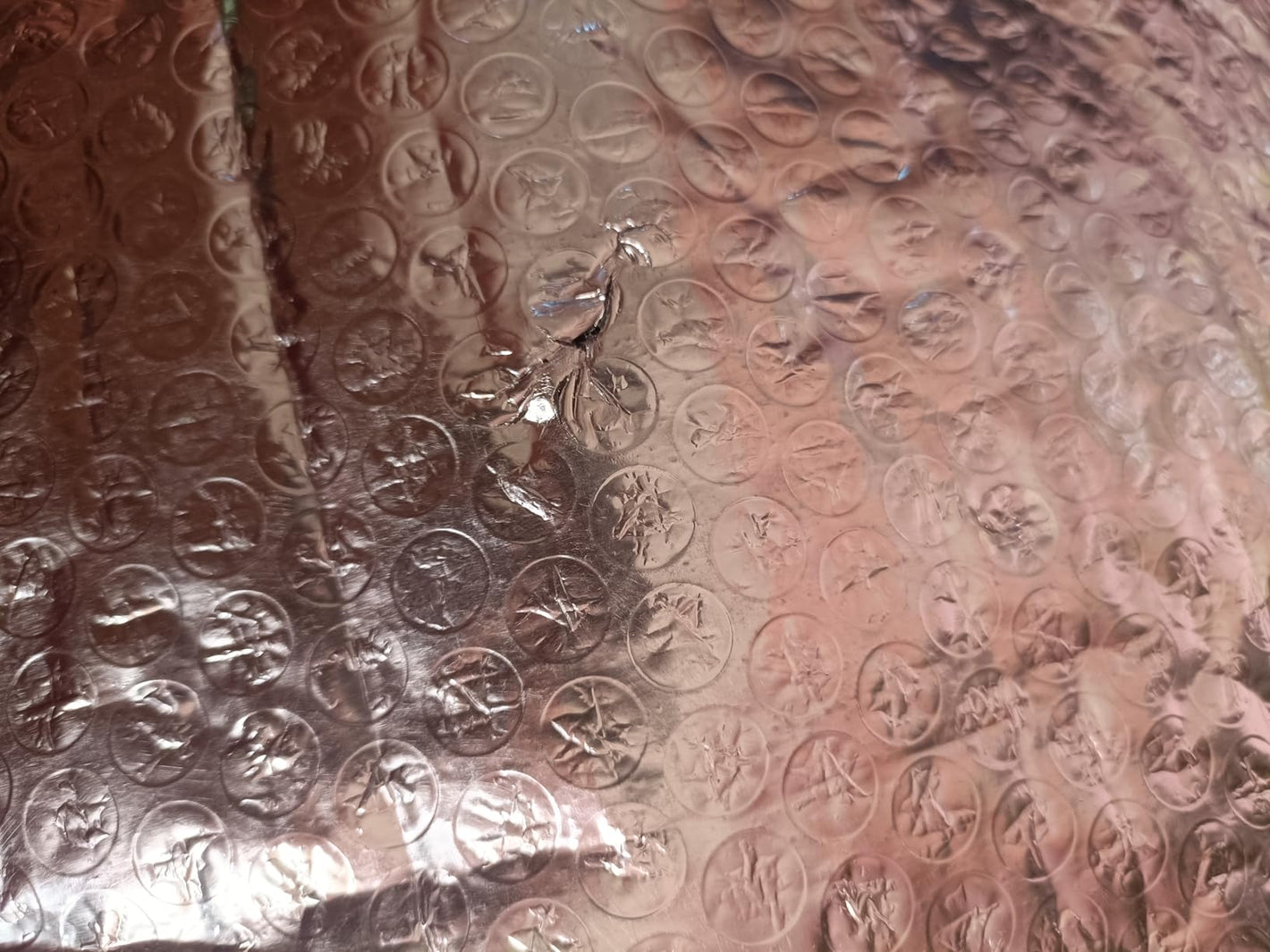 A close-up of a metallic copper or rose-gold textured surface with a circular embossed pattern and reflective highlights.
