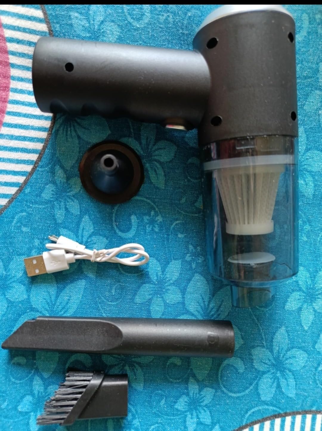 Black handheld vacuum cleaner with attachments on a blue floral-patterned surface