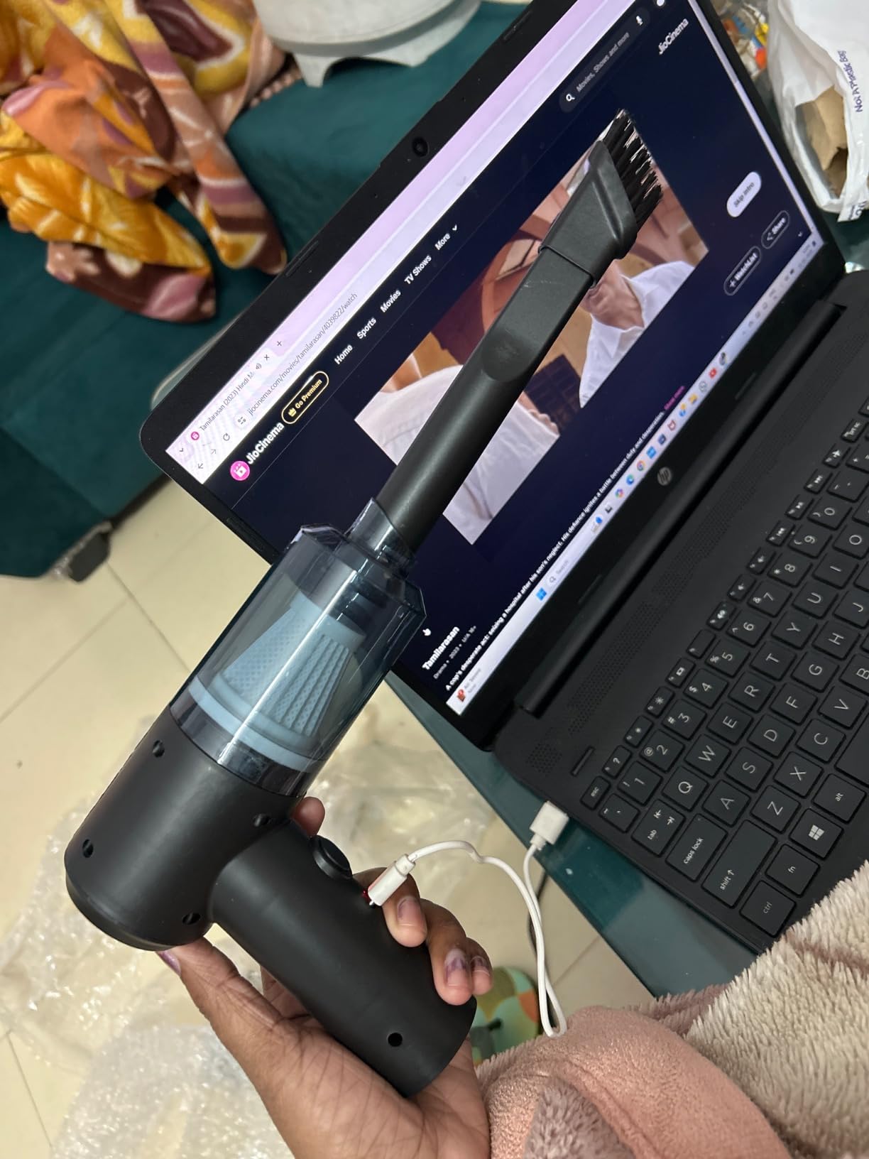 Person holding a handheld vacuum cleaner in front of a laptop displaying a website.
