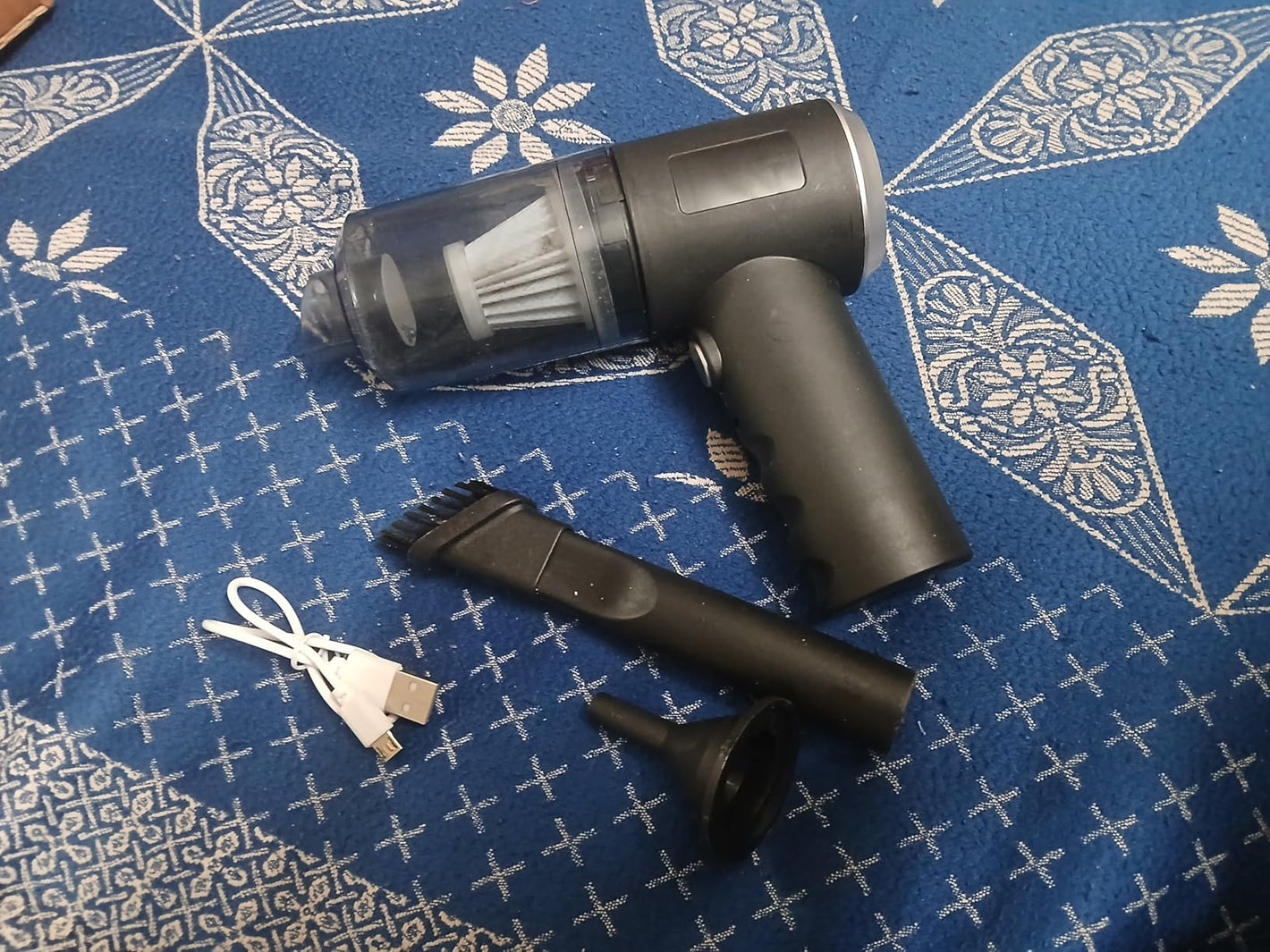 Handheld vacuum cleaner with attachments on a blue patterned fabric background