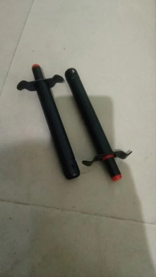 Two black cylindrical training weapons with red tips and black wing-like accents, lying on a light beige tiled floor.