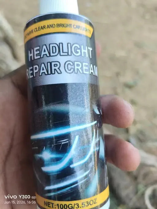 A hand holding a tube of headlight repair cream outdoors. The tube is black with a silver label, yellow accents, and a graphic of a car headlight.