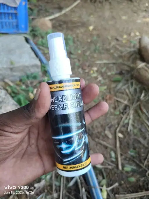 A hand holding a spray bottle of headlight repair cream outdoors on a dirt ground with a blue basket in the background.