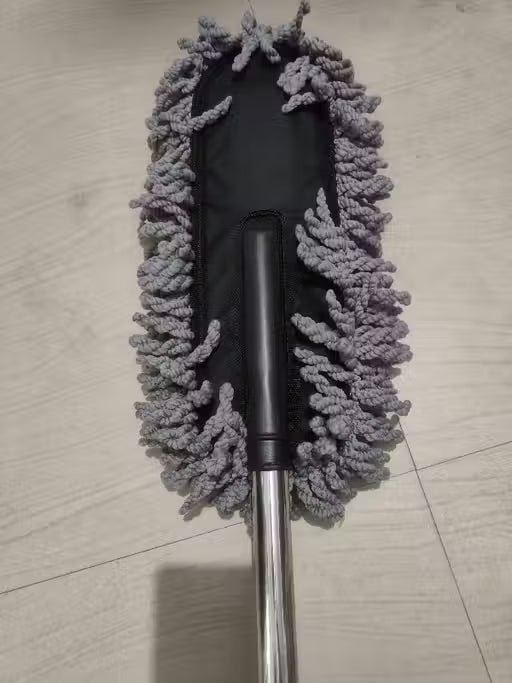 A microfiber duster mop head with gray textured cleaning fibers and a black central body, attached to a silver metal handle, shown on a light wood floor.