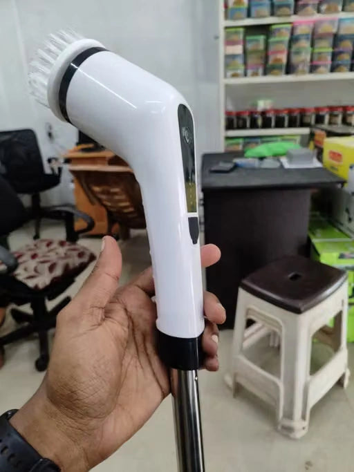 A hand holding a white handheld electric steam cleaner with a metal wand, set against a blurry background of a retail store.