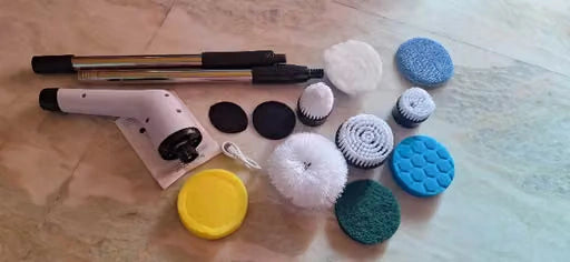 A set of rotary tool accessories laid out on a beige marble surface, including a white and black rotary hammer, two black metal rods, several circular and spiral sanding/buffing discs in blue, white, green, and black, and a yellow lid.
