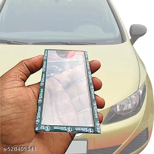 A hand holding a rectangular mirror with a dark green border printed with 'Silicon' repeatedly, set against a blurred car background.