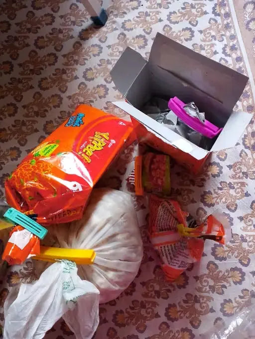 A pile of assorted household or grocery items on a patterned floor, including a large orange bag, a white plastic bag, a cardboard box, and several small packaged items.