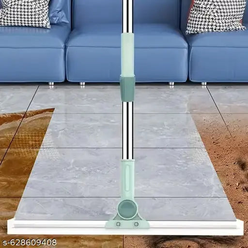 A floor squeegee with a mint green and white handle and a silver metal extension pole, shown on a gray tiled floor in front of a blue sofa.