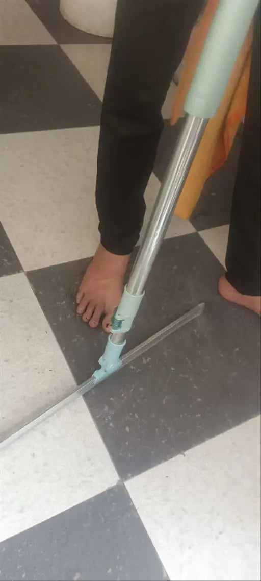 A person using a squeegee to clean a black and white checkered floor, with bare feet visible.