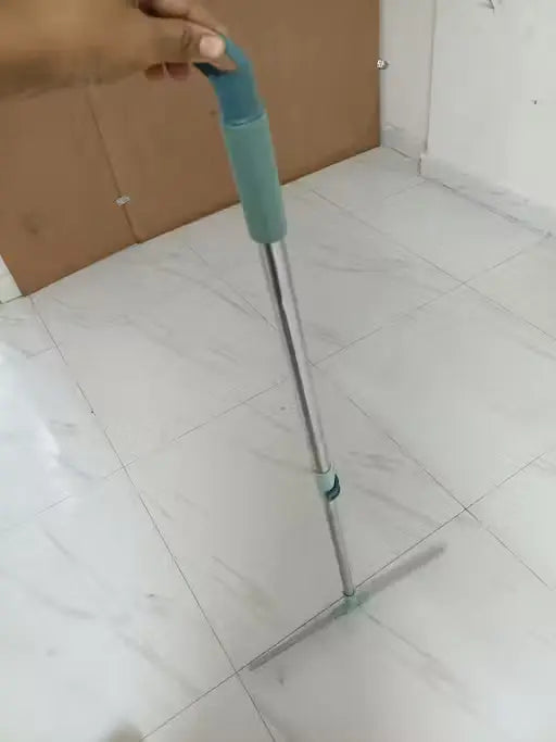 A long-handled squeegee with a mint green and teal handle and a silver metal shaft, being held by a hand on a white tiled floor.