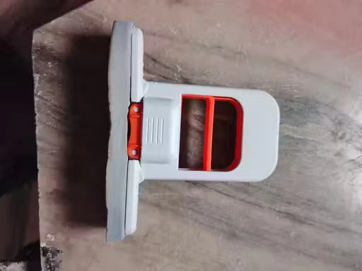 A white plastic tool with a red accent and a gray textured pad, photographed on a gray-brown wood surface.