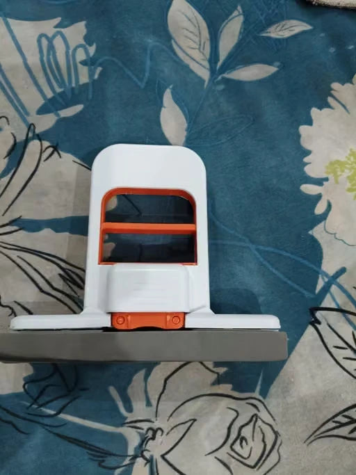 A white and orange handheld vacuum cleaner head with a gray floor brush bar, resting on a blue floral patterned fabric surface.