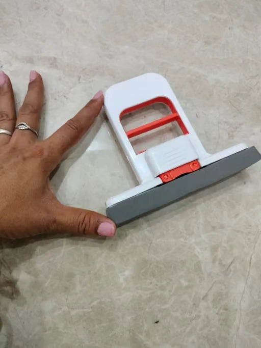 A hand-held tool with a white plastic body, red inner frame, and gray metal blade, shown on a beige marble-like floor next to a person's hand for scale.