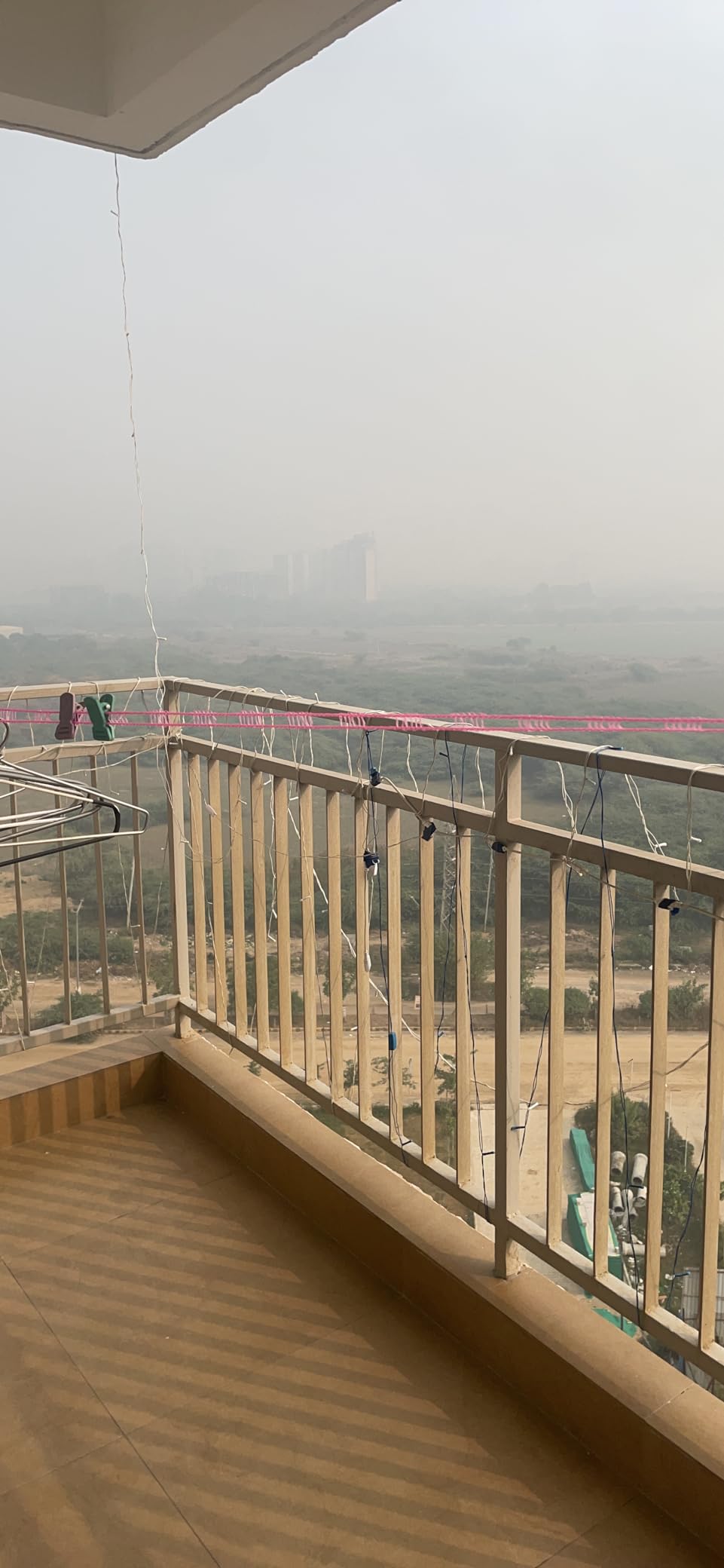 Balcony with wooden floor and railing overlooking a cityscape on a foggy day.