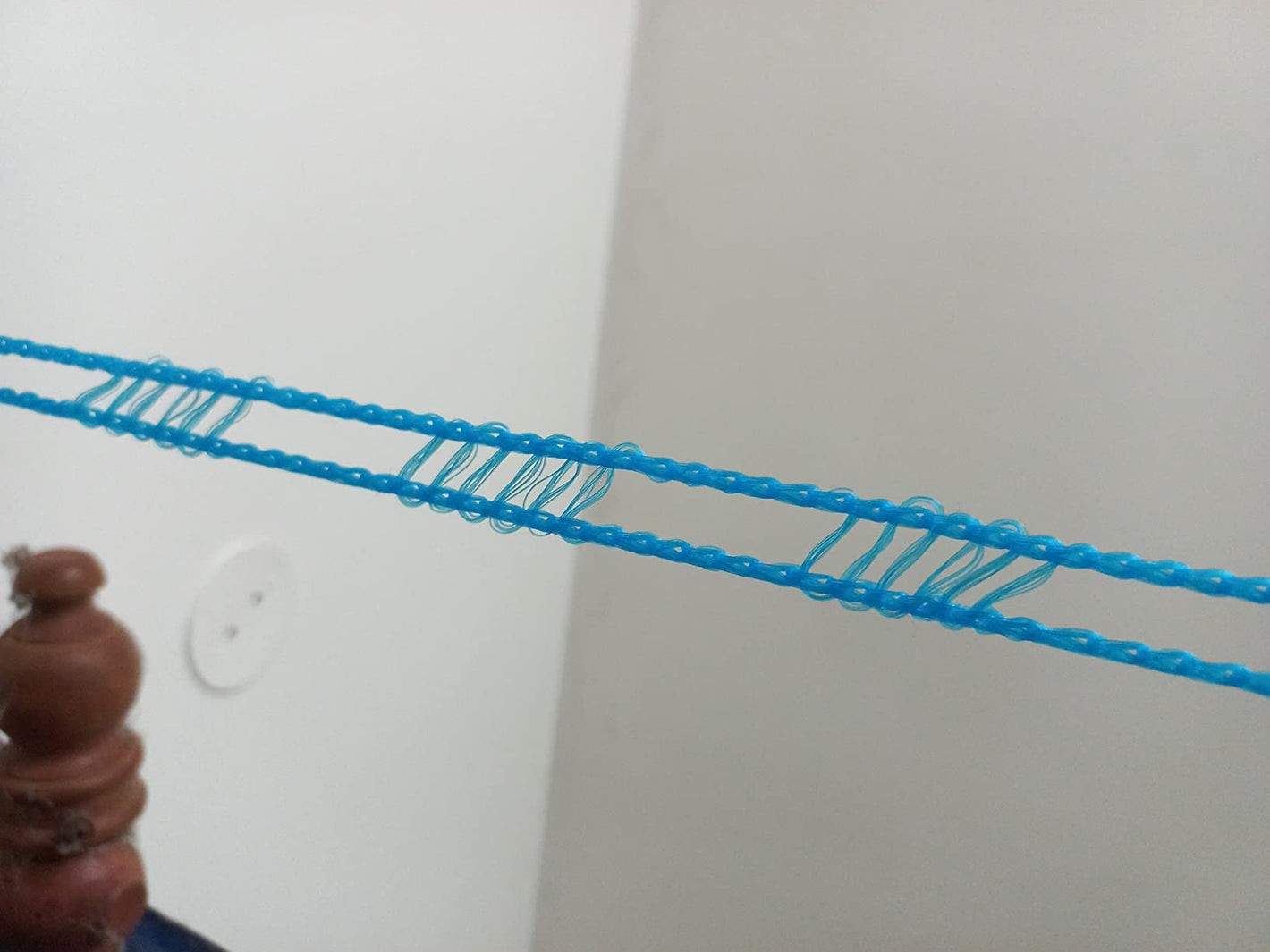 Blue cord draped over a white wall with a wooden object in the foreground.