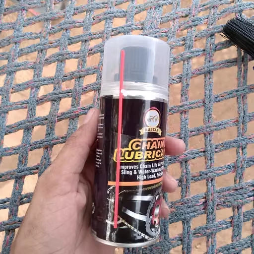A hand holding a can of Australian Chain Lubricant over a gray woven mesh background.