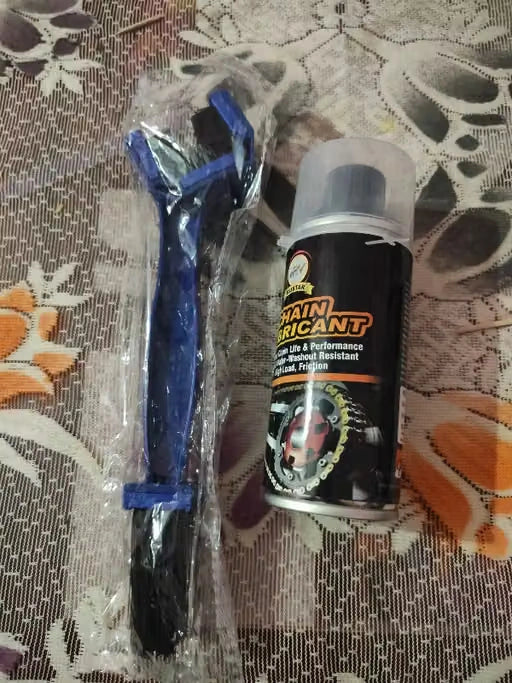 A can of black chain lubricant next to a blue plastic brush wrapped in clear plastic, placed on a patterned brown and white fabric surface.
