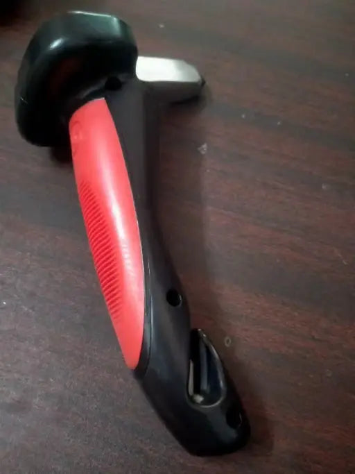 A handheld tool with a black and red ergonomic handle and a silver metal head, resting on a dark brown wooden surface.