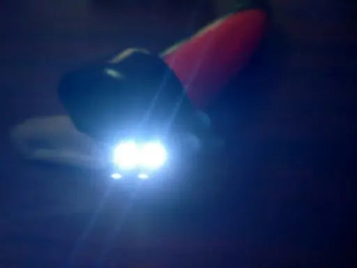 A bicycle light with a black body and a red accent, shown glowing with bright white LED lights on a dark background.