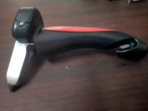 A black and red handheld tool with a white metal blade, resting on a dark wooden surface.