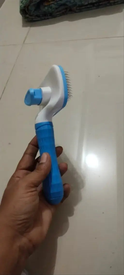 A hand holding a blue and white pet grooming brush with soft bristles, set against a tiled floor background.