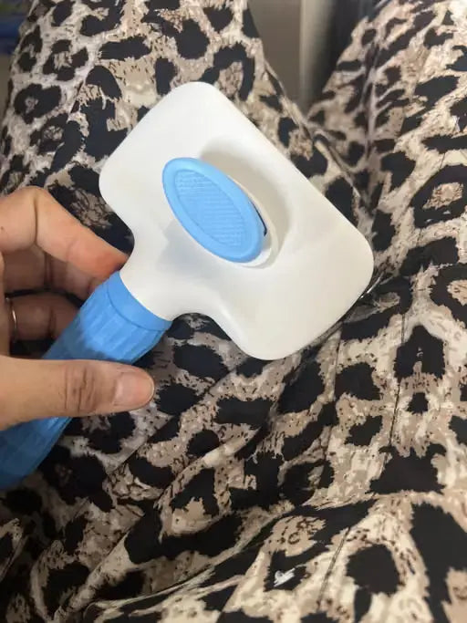 A hand holding a white and blue pet grooming brush against a leopard-print fabric background.