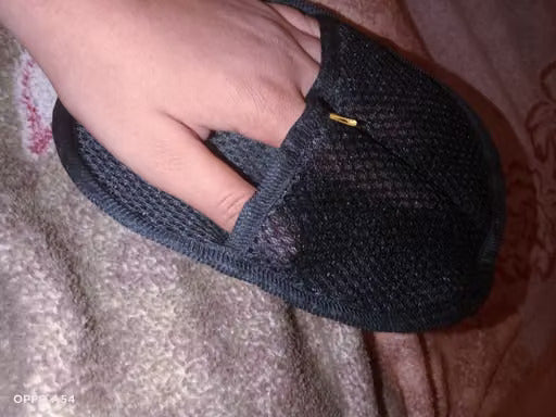 A close-up shot of a hand wearing a black knit slipper or sock with a small gold pin detail, resting on a textured blanket.