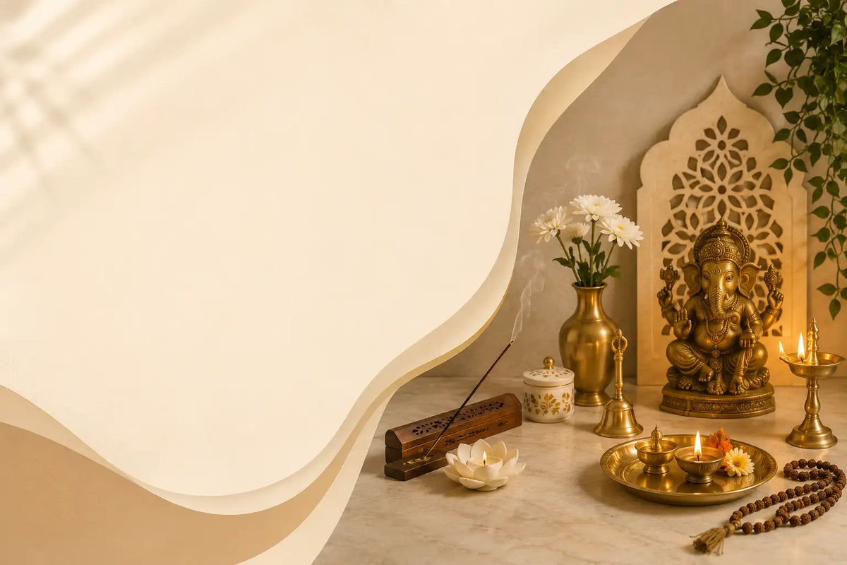 A styled interior scene with warm cream wavy architectural panels, a brass Ganesha statue, a brass incense holder with a smoking incense stick, a brass vase with white flowers, a lit diya, and a beaded necklace on a marble surface.