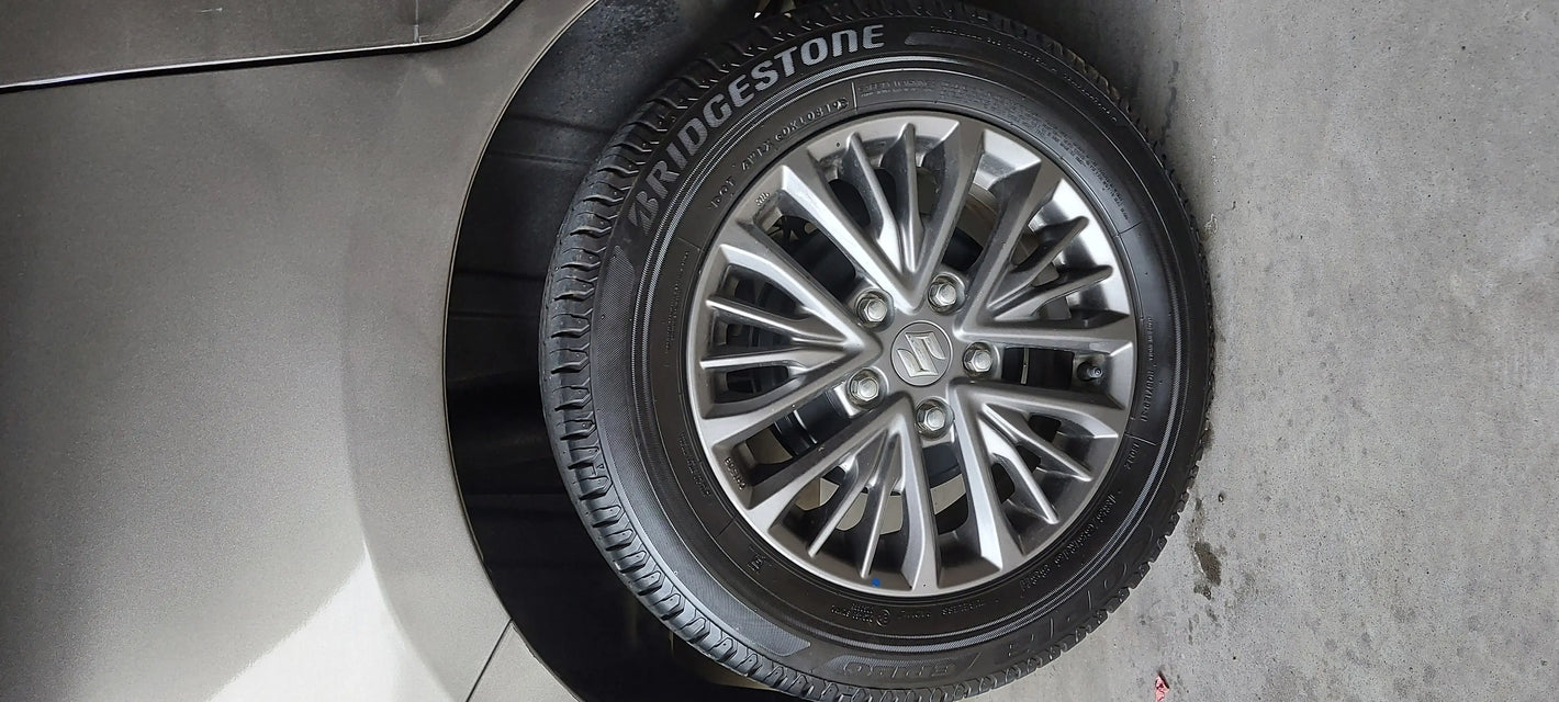 Close-up of a silver multi-spoke alloy wheel and Bridgestone tire mounted on a vehicle, with part of the silver car body visible on the left and a concrete floor on the right.