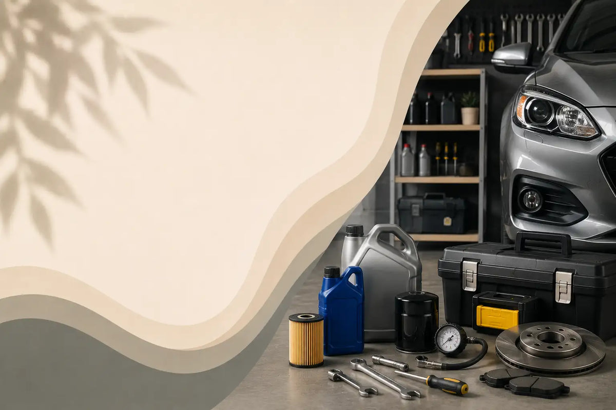 A garage scene with automotive repair tools and parts arranged on the floor, including an oil can, filter, wrenches, a toolbox, brake disc, and other maintenance items, with part of a silver car visible in the background.