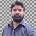 A man with a beard and a red tilak on his forehead, wearing a dark blue-gray button-up shirt, shown against a gray and white checkerboard background.